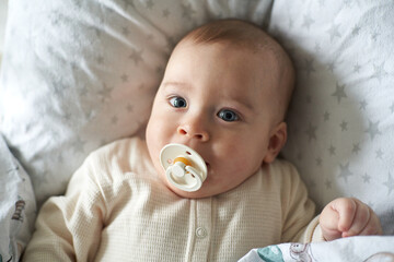 baby with pacifier in bed before sleep. Pretty six-month old baby boy. Realistic home portrait