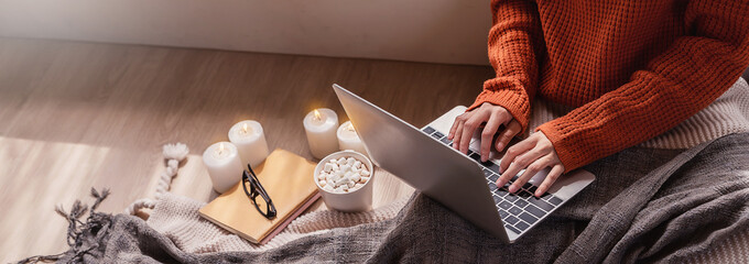 Top view of woman in sweater hands typing computer with cup of hot chocolate winter time at home. Flat lay of girl relaxing in cold winter, stay work at home, pandemic concept banner