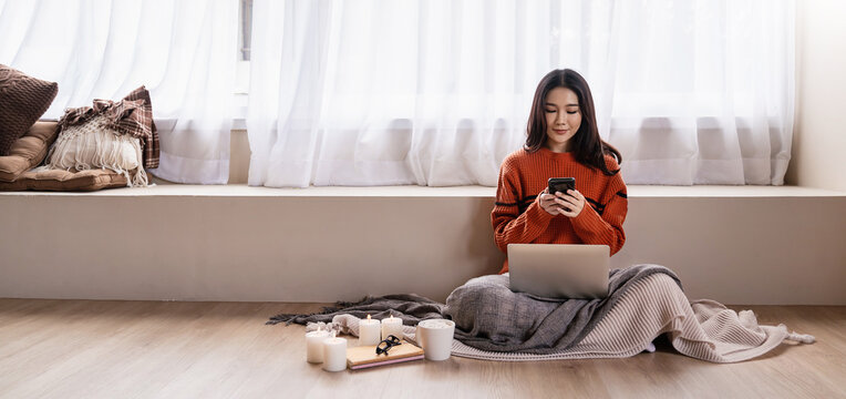 Asian nerd glasses woman work with computer cell phone on the floor. Warm woolen sweater in cold autumn or winter weekend, warm drink. Sme small business work from home online technology.