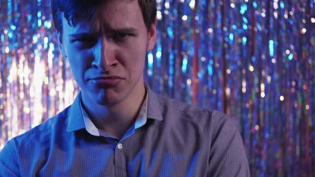 Party disappointment. Offended man. Neon light portrait. Sad guy crying with childish expression posing on blinking rainbow festive silver cascade decoration.