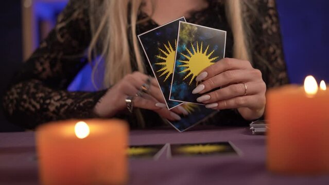 Fortune teller hands holding THE SUN card and tarot cards on table near burning candles in candle light.Tarot cards spread on the table. Forecasting