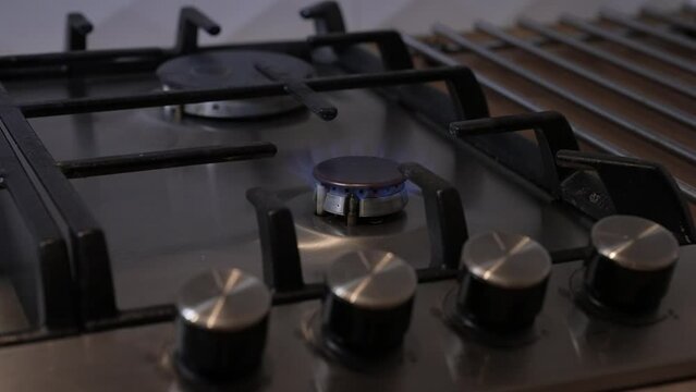 Close-up of hand turning on gas stove flame. Close-up of hand turning on gas stove flame. Metal gas stove. Male hands turning on gas stove through electric lighter
