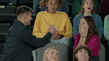 Kisscam moment - female agrees to marriage proposal during a game. Television like camera zoom. Fans attending a sports event, watching themselves on a jumbotron screen