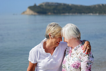 Fototapeta na wymiar coppia di signore anziane abbraccia affettuosamente sulla riva del mare