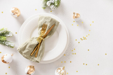 Christmas festive table setting with white plate, golden balls on white background. View from above. Copy space. Xmas dinner.