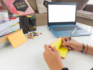 mockup image, Laptop computer with blank screen with a woman taking notes on yellow paper with pen in modern home room. mockups laptop
