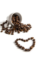Spilled coffee beans from a cup with a heart pattern.