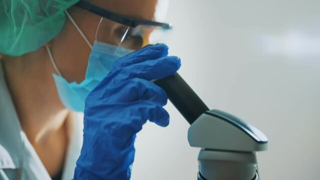 Scientist in medical mask working with microscope in lab.