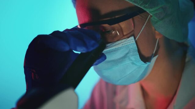 Scientist in medical mask working with microscope in lab.