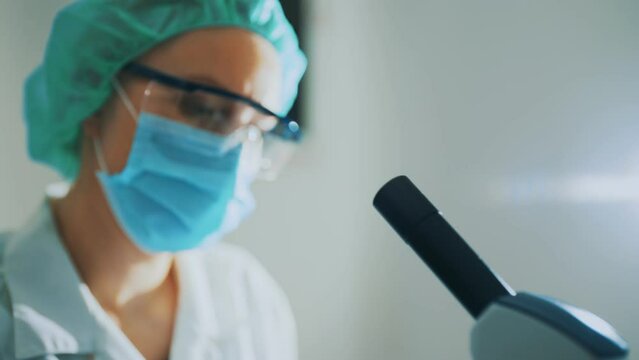 Scientist in medical mask working with microscope in lab.