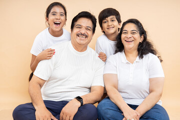 Happy indian grandparents with kids wearing white casual t-shirt sitting together isolated over beige background.