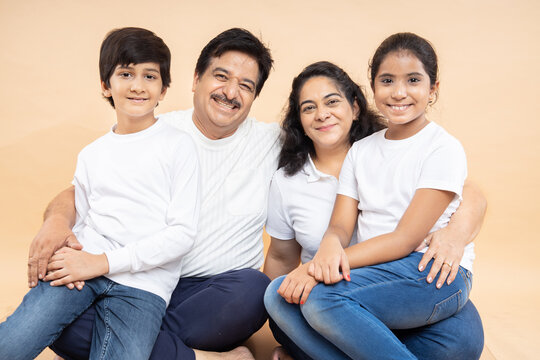 Happy Indian Grandparents With Kids Wearing White Casual T-shirt Sitting Together Isolated Over Beige Background.
