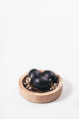 Eggs painted black on white background. Nest containing three egg with beautiful gypsophila flowers. Minimal Easter concept with copy space for text.