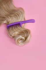 Purple comb in a curl of hair. Blond hair on a pink background. Hair close-up.