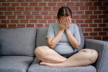 Stressed fat woman sitting on the sofa in the living room, feeling disappointed. She covered her...