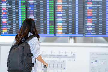 Young Asian female tourist looking at flight schedule for travel. Portrait in back view.