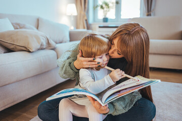 Shot of a young beautiful mother reading a book to her adorable daughter in bed at home. Mother and daughter lying on warm floor reading book. Little girl working her homework with mother.