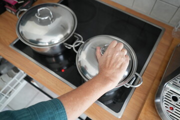 Woman cooking in the kitchen with her hand on a pan lid. Ideal for food, home, and lifestyle blogs