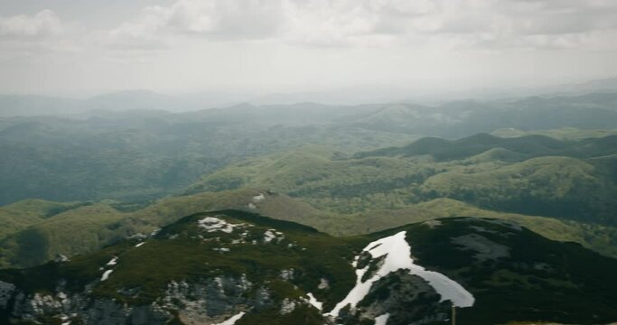 A view from the peak of mountin Snežnik into the valley. Green mountains with a small patches of white.