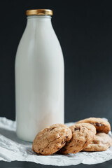 Homemade cookies with pieces of chocolate next to a bottle of milk on a dark background