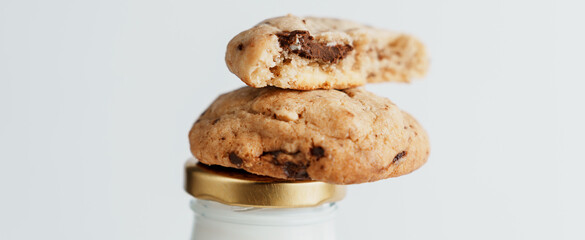 Cookies with pieces of chocolate lying on a bottle of milk on a white background