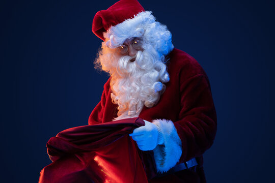 Portrait of old santa claus with glasses and bag with gifts against dark background.