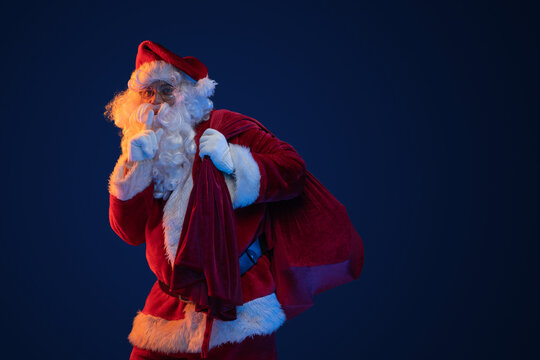 Studio shot of santa dressed in red clothes carrying bag against dark background.