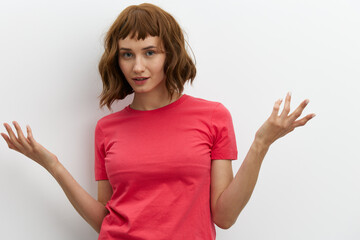  emotional, surprised woman poses standing on a white background in a pink T-shirt, actively gesticulating with her hands. Horizontal photo with an empty space for inserting an advertising layout