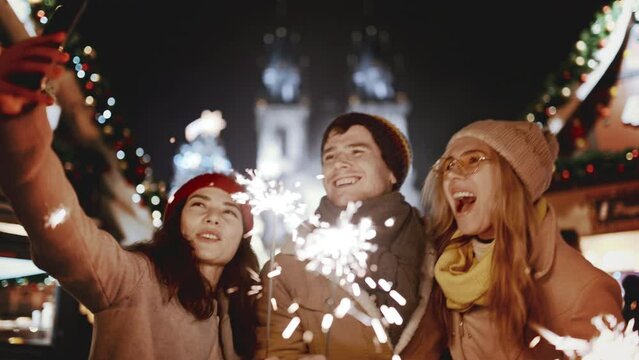 People hands in the dark waving sparklers on backdrop of garland. new year, holiday, Happy men and women celebrate Christmas, birthday, party. Taking selfie on phone with firework Smiling. Night Shot
