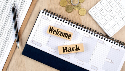 WELCOME BACK word written on wooden block on planner with coins, clipboard and a calculator