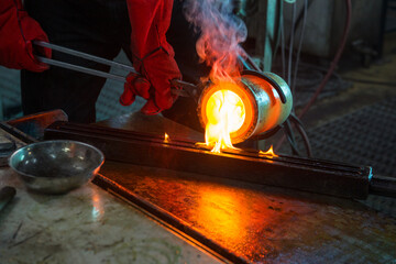 The master's hands in special red refractory mittens pour molten gold from a refractory glass into a mold.