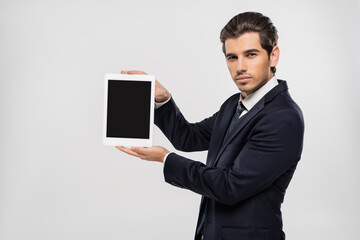 young businessman in suit holding digital tablet with blank screen isolated on grey