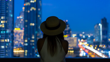Woman tourist enjoying her urban city skyline of the nightlife view from the hotel room balcony for...