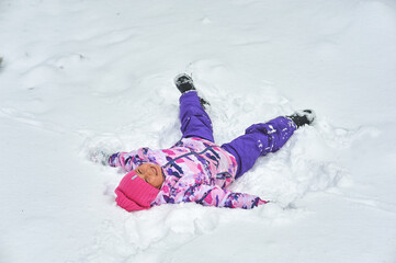 Happy little girl rejoices in winter lying on the snow
