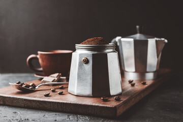 Moka coffee pot filled with brown ground coffee on dark wooden board, prepare to brewing Italian espresso