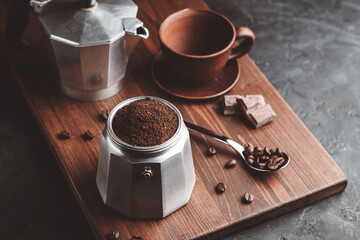 Moka coffee pot filled with brown ground coffee on dark wooden board, prepare to brewing Italian espresso