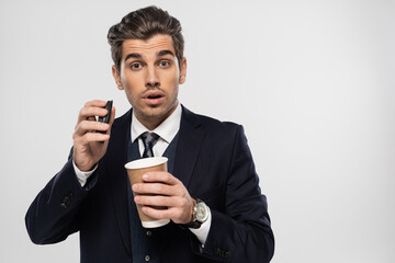 surprised and sleepy businessman holding paper cup with takeaway drink isolated on grey
