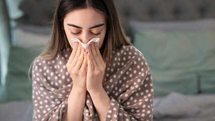 Young sick woman blowing her nose while in bed