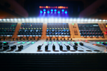 Selective focus on sliders of professional audio mixing console against colorful spotlights..