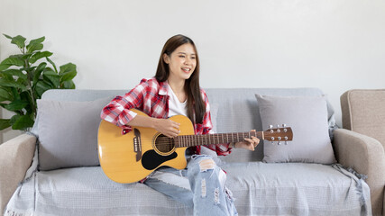 Asian female artist playing the guitar and singing happily in the living room, Relaxation with...