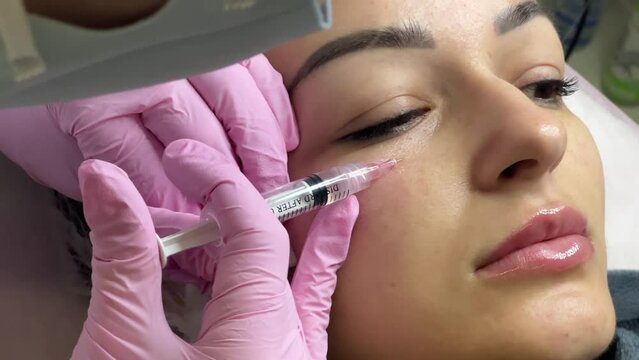Face mesotherapy procedure in a beauty salon. Beautician doctor makes injections into the skin of the face of a young beautiful woman. Mesotherapy, biorevitalization. Cosmetology. Selective focus.