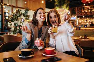 Two best friends sitting in coffee bar or restaurant after shopping and happily talking together.