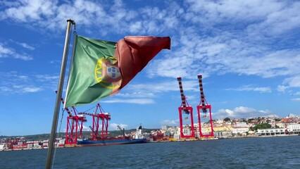 ortugal flag waving in the back of a tour boat passing by the Port of Lisbon, Portugal - Powered by Adobe
