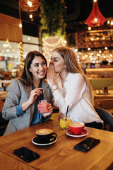 Two best friends sitting in coffee bar or restaurant after shopping and happily talking together.