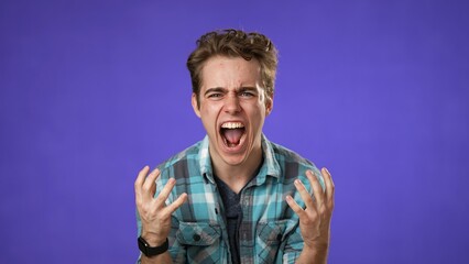 Fototapeta premium Angry frustrated despair upset with clenched fists portrait of young man 20s isolated isolated on purple background.