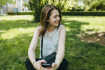 Obraz premium Happy beautiful young Caucasian girl with smart phone outdoors on sunny summer day texting and smiling