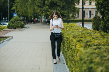 Happy beautiful young Caucasian girl with smart phone outdoors on sunny summer day texting and smiling