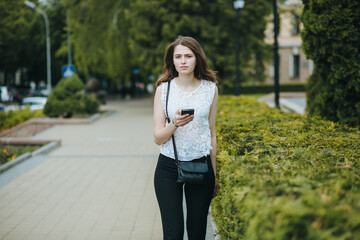 Happy beautiful young Caucasian girl with smart phone outdoors on sunny summer day texting and smiling