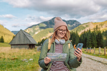 Naklejka na ściany i meble Active young woman holding reading a map while taking a hiking break, having fun and relaxing while spending autumn day outdoors. 