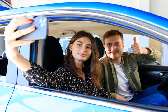 Photo in a new car. A young couple takes a selfie. Buying a new luxury car at a dealership